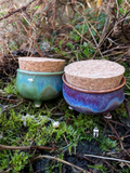 Two ceramic containers with cork lids on a natural background
