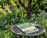 Book titled 'Perennial Gardening' on a garden table surrounded by plants and flowers