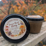 Jar of 'Immune Boost Honey' with a decorative label on a wooden surface with blurred autumn foliage in the background.