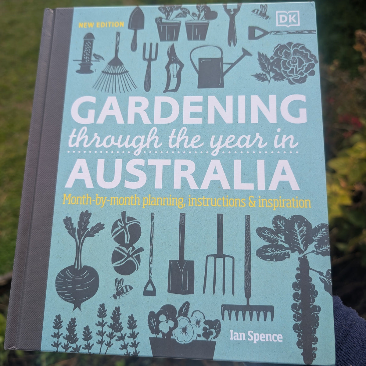 Book titled 'Gardening through the year in Australia' by Ian Spence with gardening-themed illustrations on a blurred natural background.