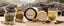 A tea and honey bundle displayed on a wooden table with a blurred mountain forest background. Visible items include a round jar labeled Healthy Gut Herbal Honey, an open jar of pale honey, a glass mug filled with tea and metal teabag, jars of loose herbs and flowers with wooden spoons, a honey dipper, cinnamon sticks, and star anise.