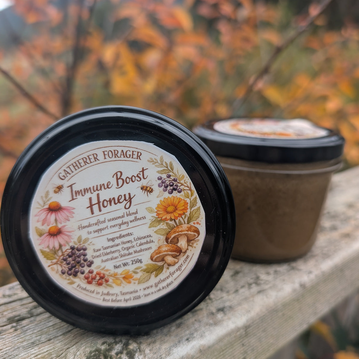 Jar of 'Immune Boost Honey' with a decorative label on a wooden surface with blurred autumn foliage in the background.