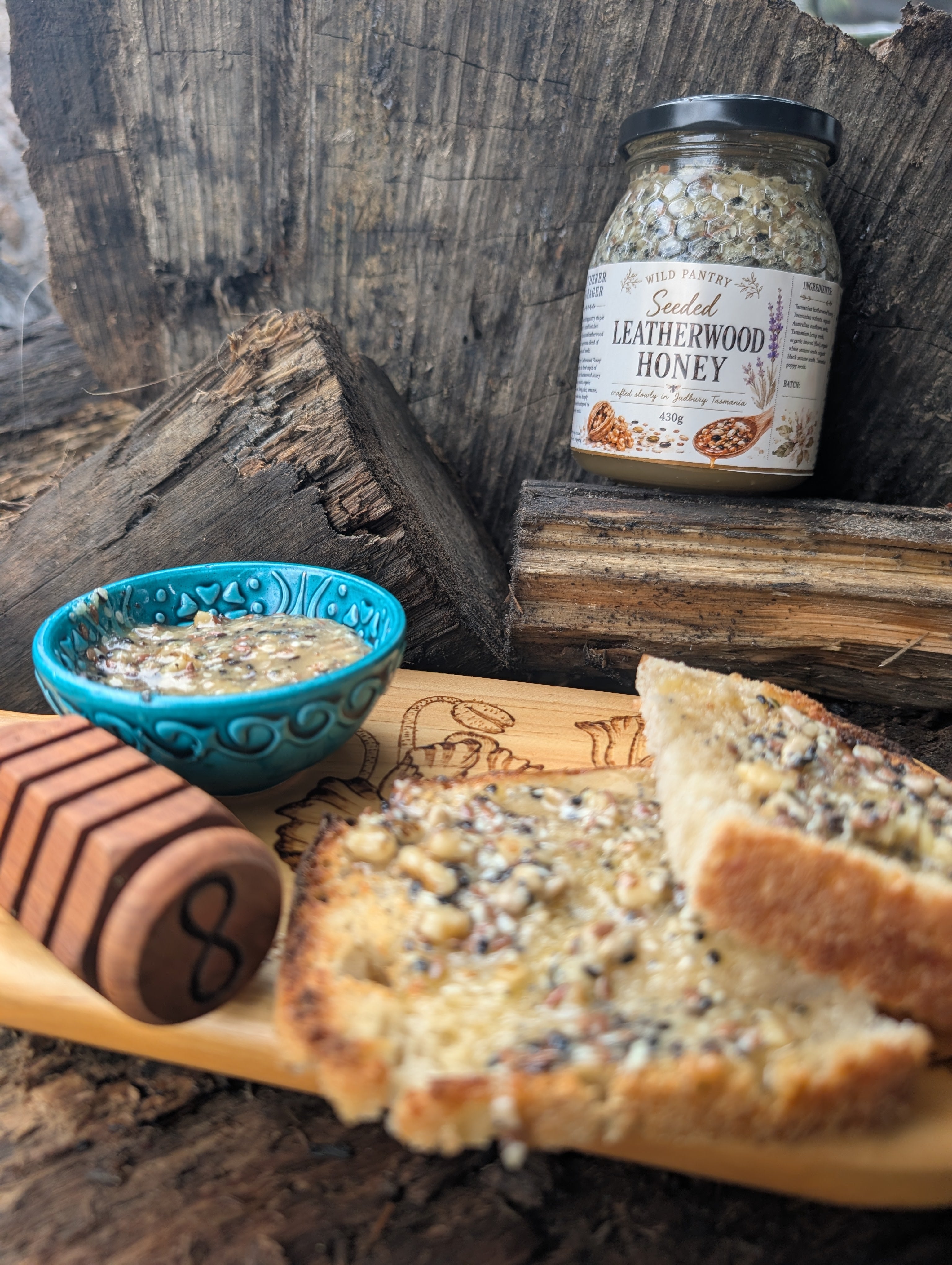 Jar of leatherwood honey, blue bowl with honey, and bread slices on a wooden surface.