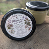 Two jars of Gatherer Forager Migraine Support herbal honey displayed on a rustic wooden surface with a blurred outdoor background.
