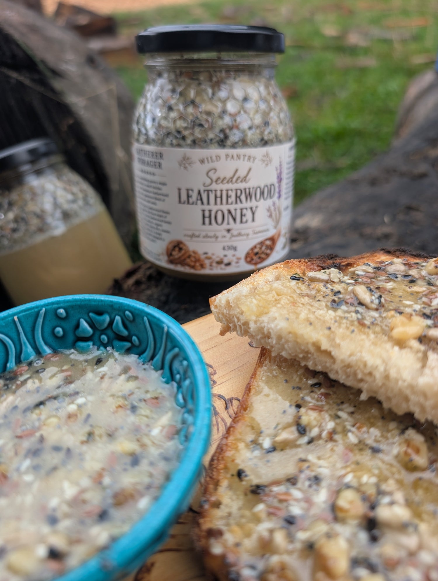 Jar of Gatherer Forager Seeded Leatherwood Honey with bread and honey on a wooden surface