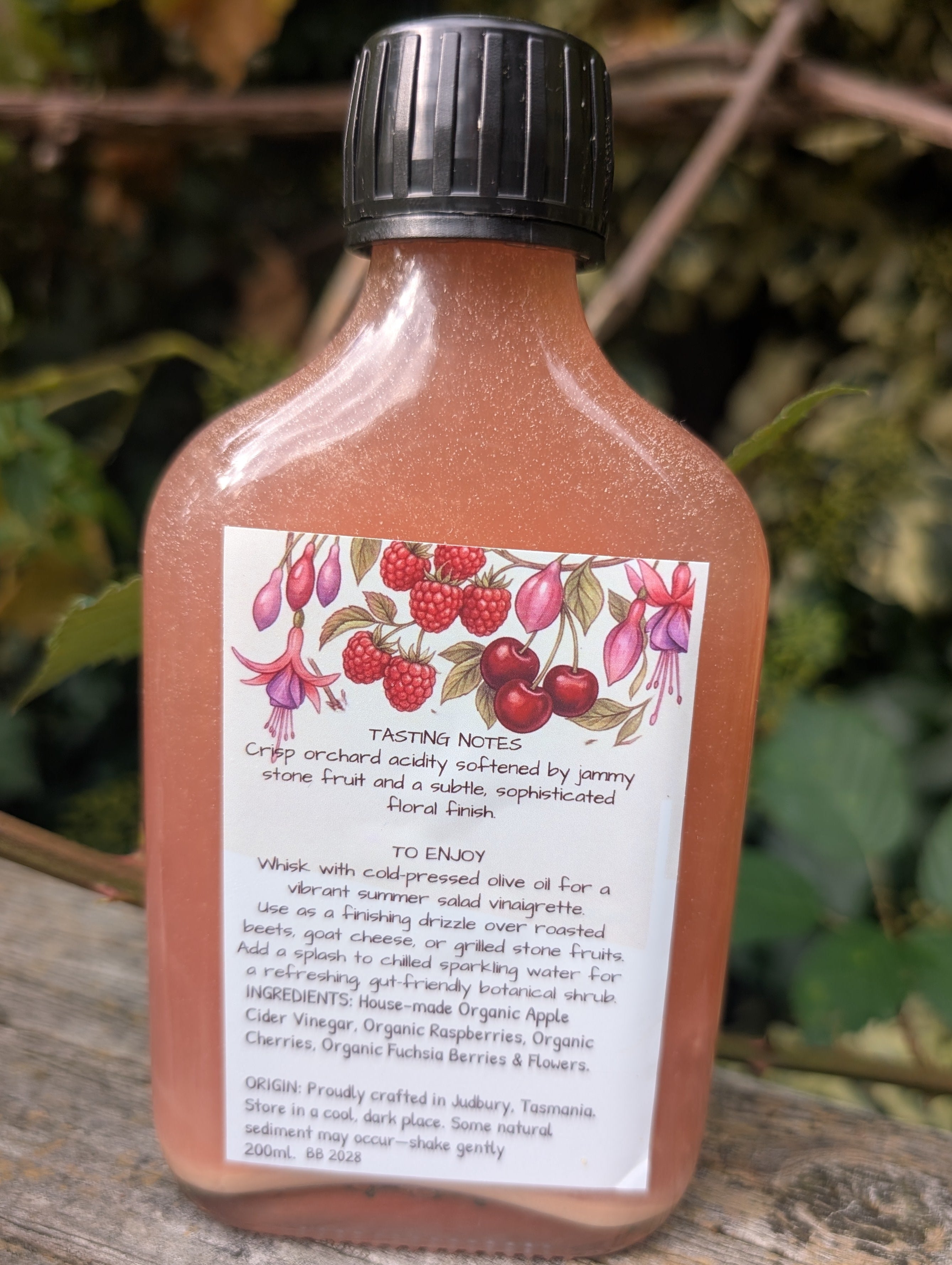 Bottle of vinegar with a label on a wooden surface and leafy background